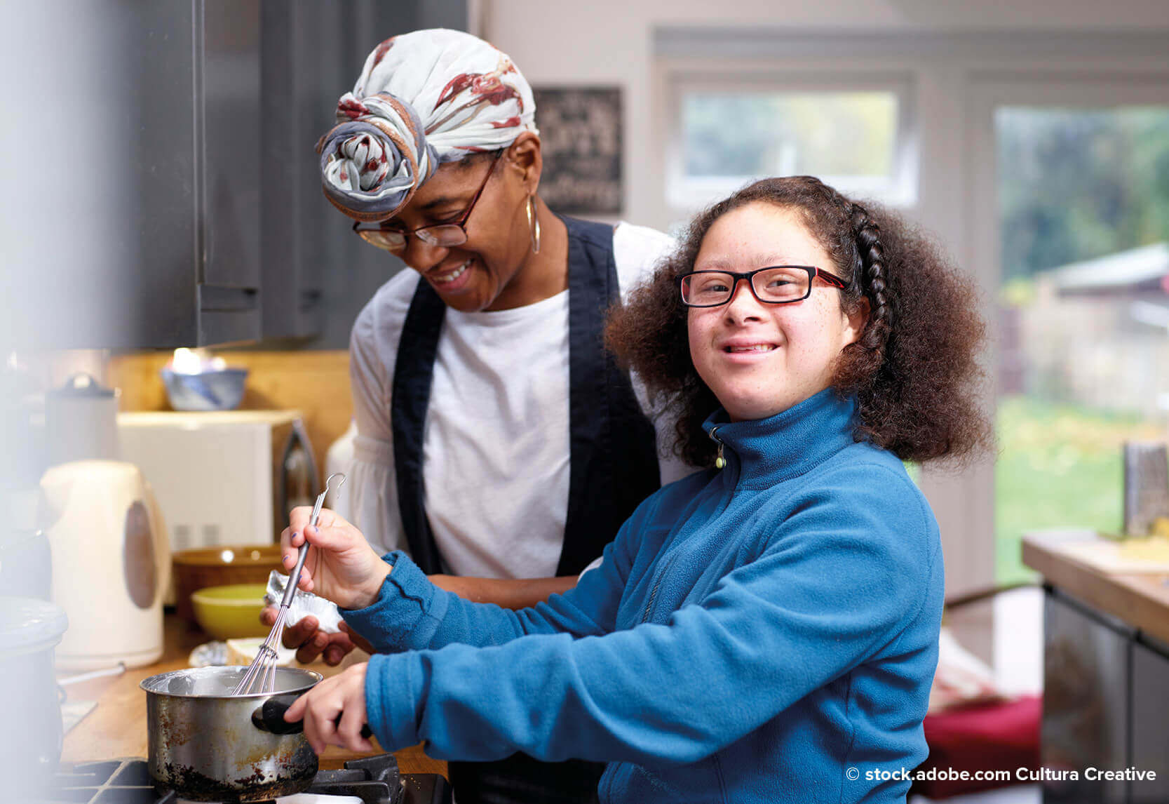 A woman with a girl stirring a pot in a kitchen