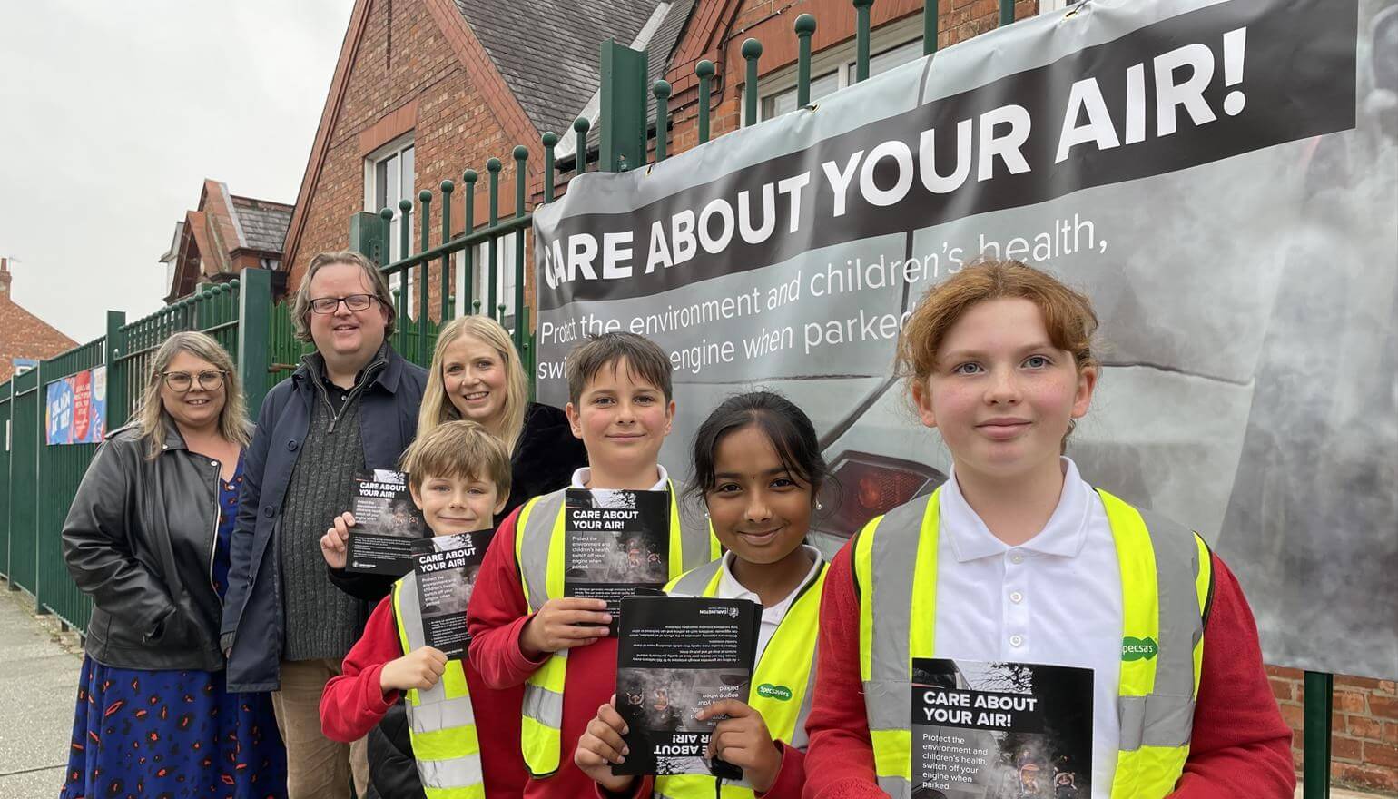 Children and adults outside school gates holding posters