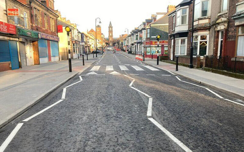 road with zebra crossing and shops on each side and clock tower at the end